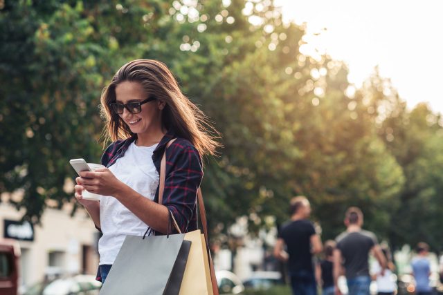 a woman holding shopping bags and looking at her cell phone.