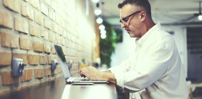 Middle Age man in glasses typing on laptop.