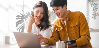 Asian couple husband and wife sitting at table at home together using online banking on laptop to view eStatements.