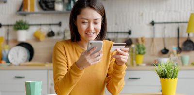 Happy woman holding debit card and phone setting up Debit Card Controls within the mobile banking app