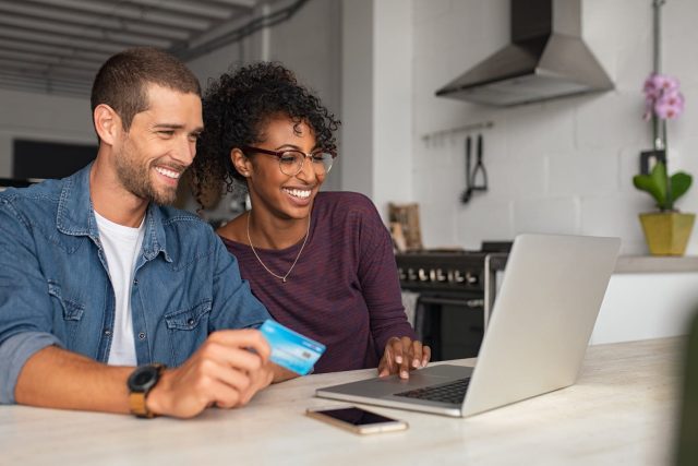 Smiling young couple making setting up activity alerts in online banking using a laptop at home.